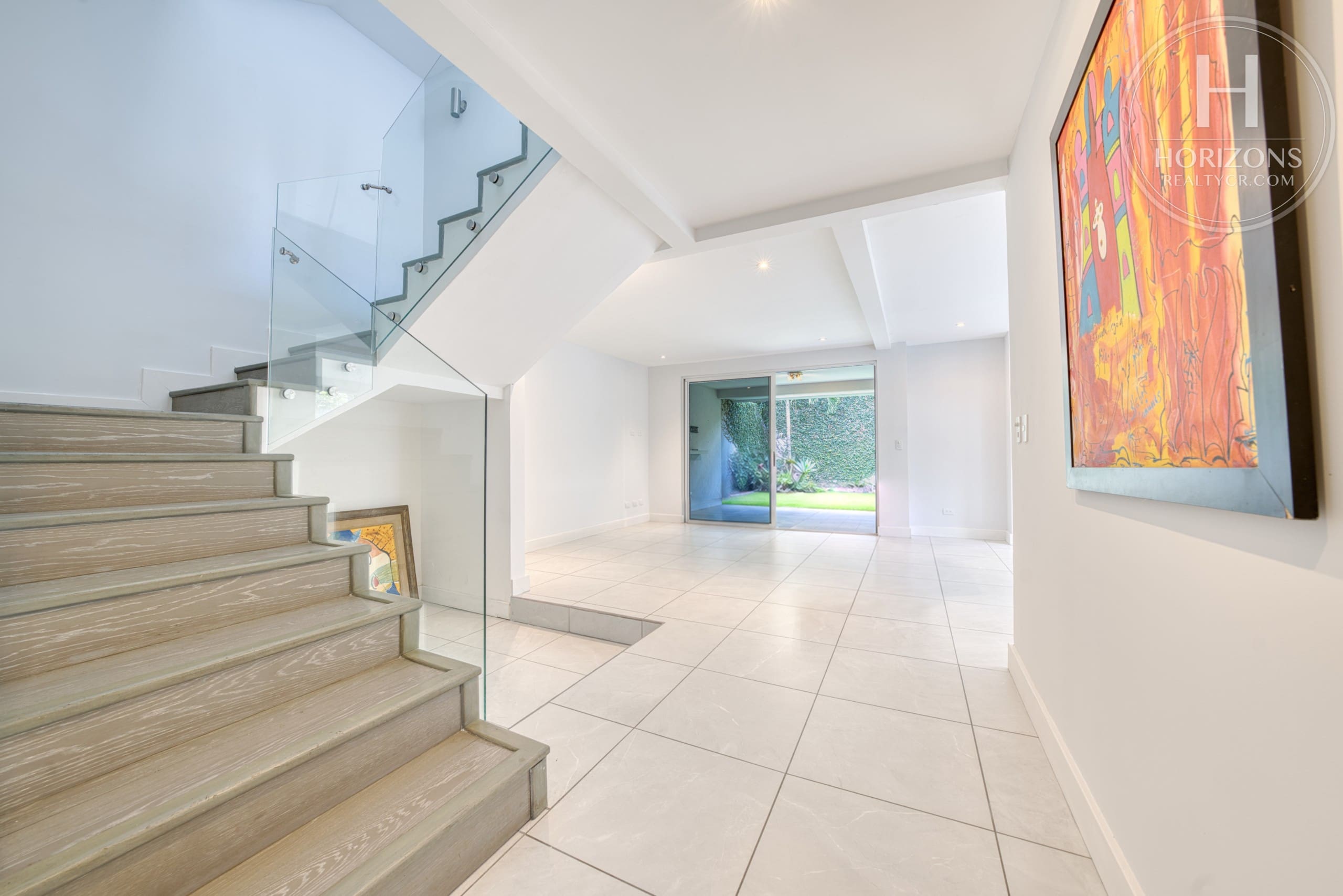 Escalera con baranda de vidrio y sala – Casa en Condominio Vistas de Escazú, San Rafael de Escazú | Horizons Realty