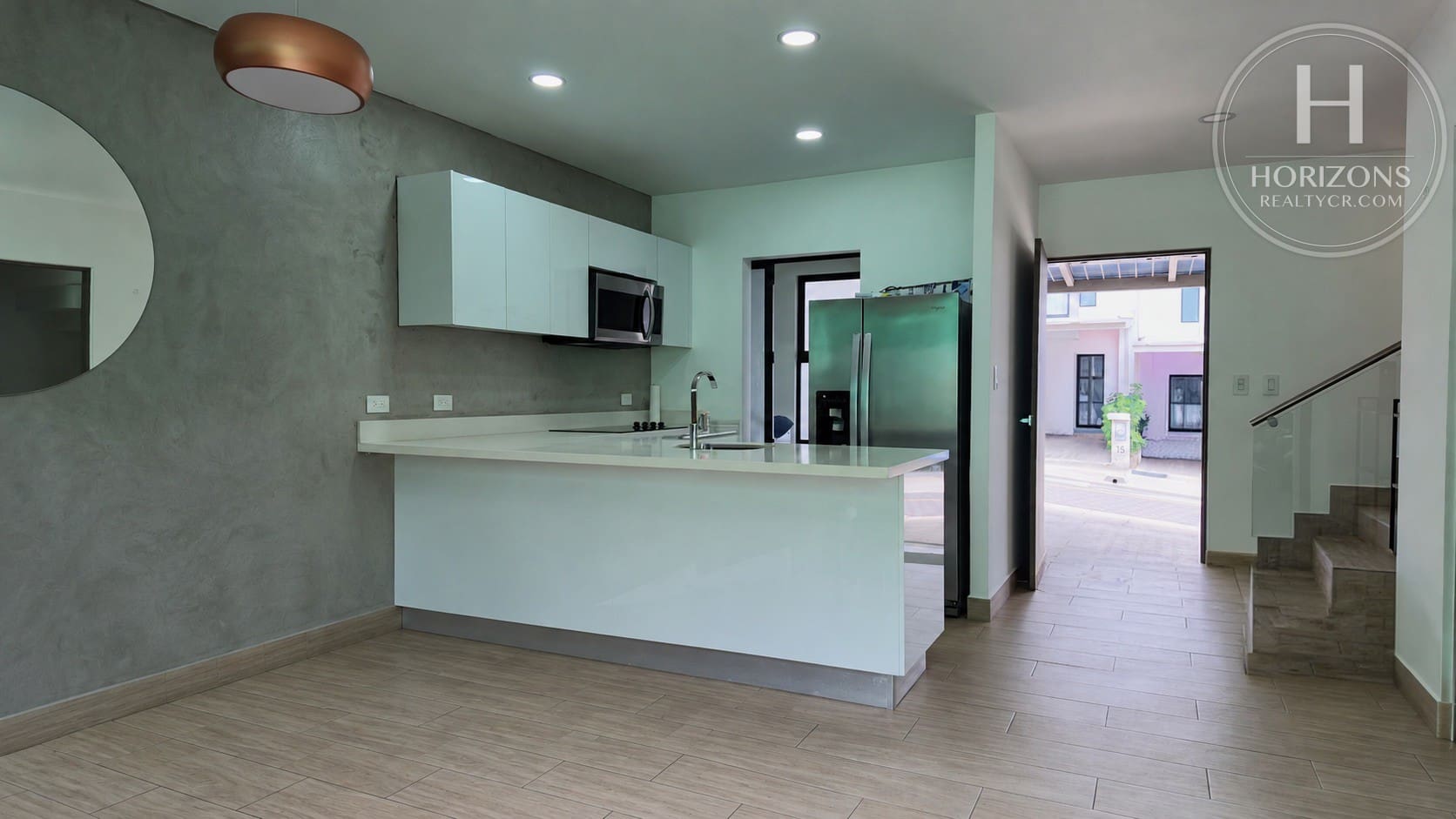 Cocina con península, gabinetes blancos y acceso a la entrada – Casa en Condominio Bali, Guachipelín de Escazú | Horizons Realty