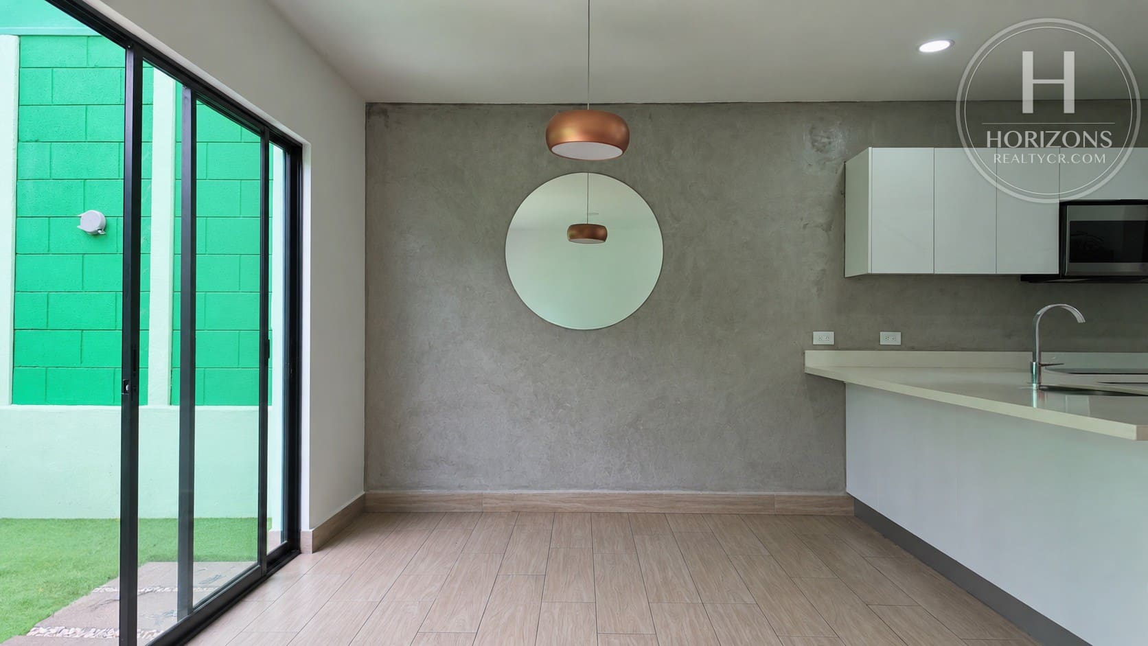 Comedor con pared de acento tipo cemento y puerta corrediza al patio – Casa en Condominio Bali, Guachipelín de Escazú | Horizons Realty
